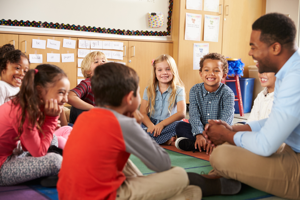 des enfants assis en cercle à l’école rient avec l’éducateur