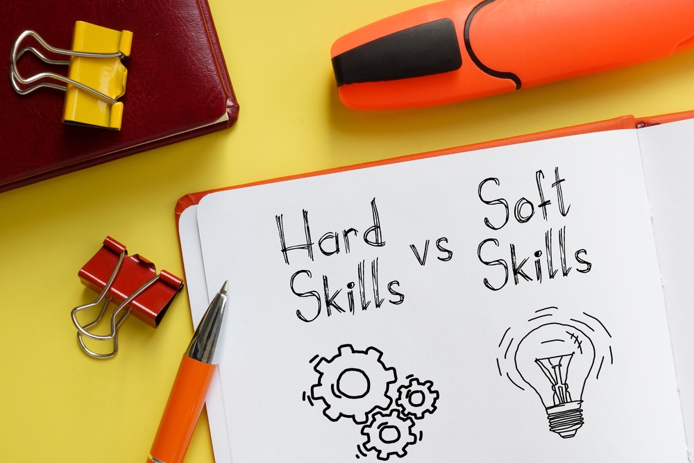 Hard skills vs soft skills écrits sur un cahier d’école montrant une icône rouages et une icône ampoule, symbole de recherche, d’idées et d’apprentissage.