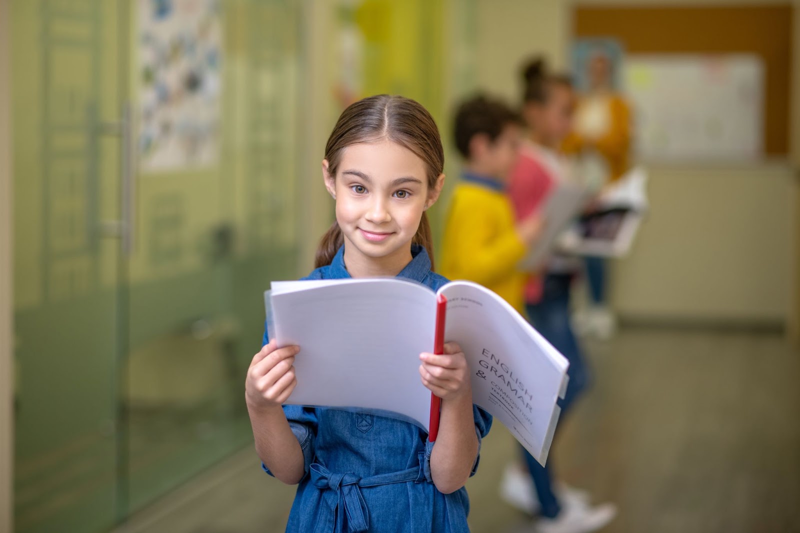 Petite fille souriante lisant son cahier de grammaire en anglais