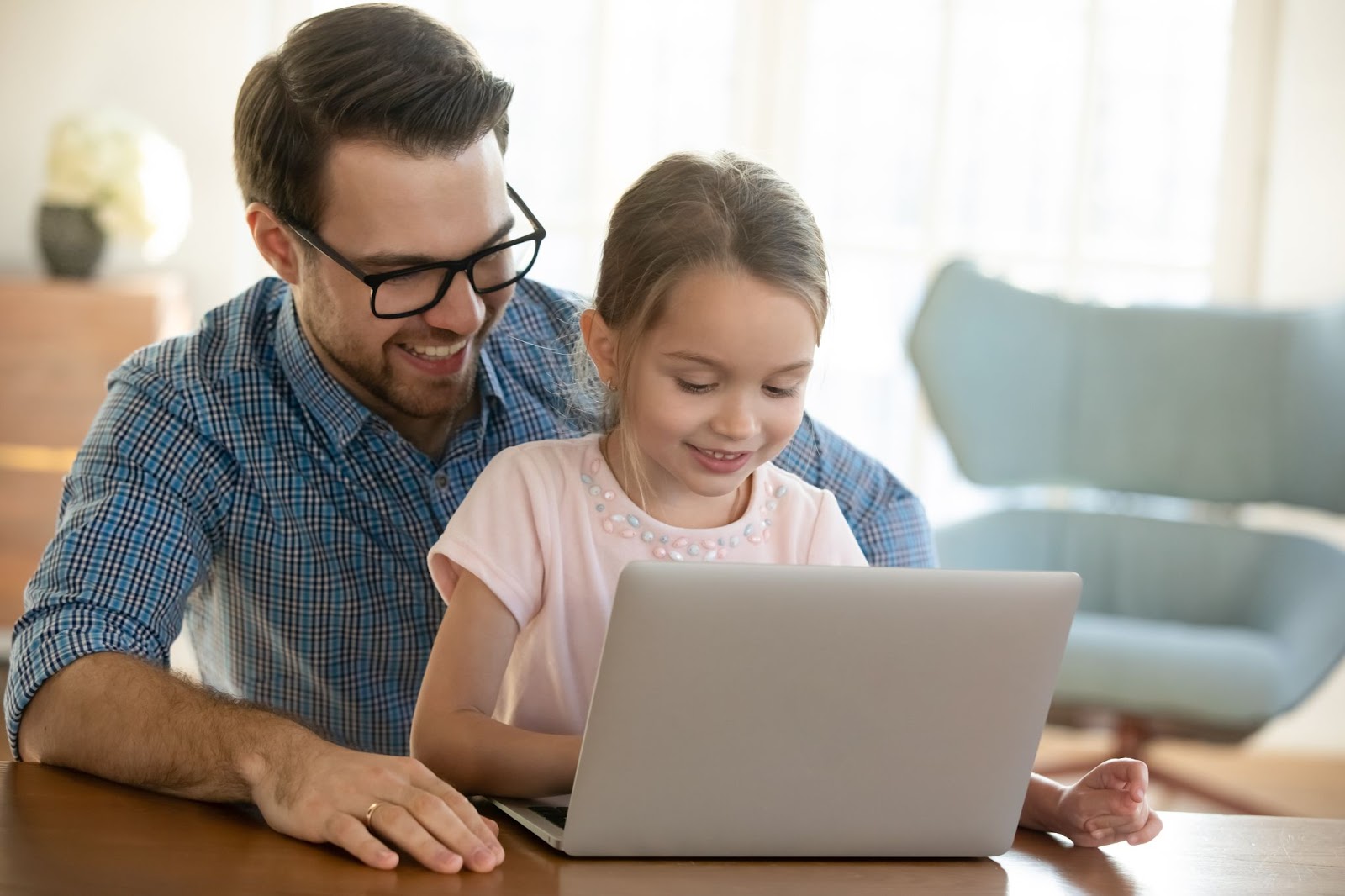 Tournage de tête sur un jeune père souriant en lunettes, brandissant une petite fille d'âge préscolaire, regardant une vidéo amusante sur ordinateur