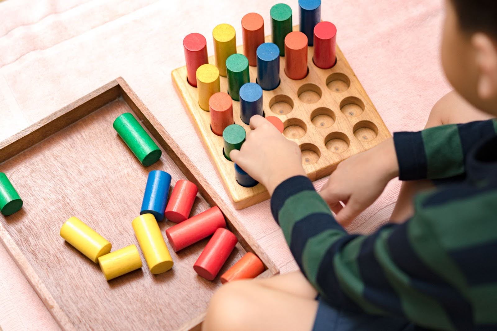 Mains d'un petit enfant Montessori (3-6) apprenant l'organisation par des blocs sensoriels en bois colorés. Jouets éducatifs, habiletés cognitives, activité Montessori.